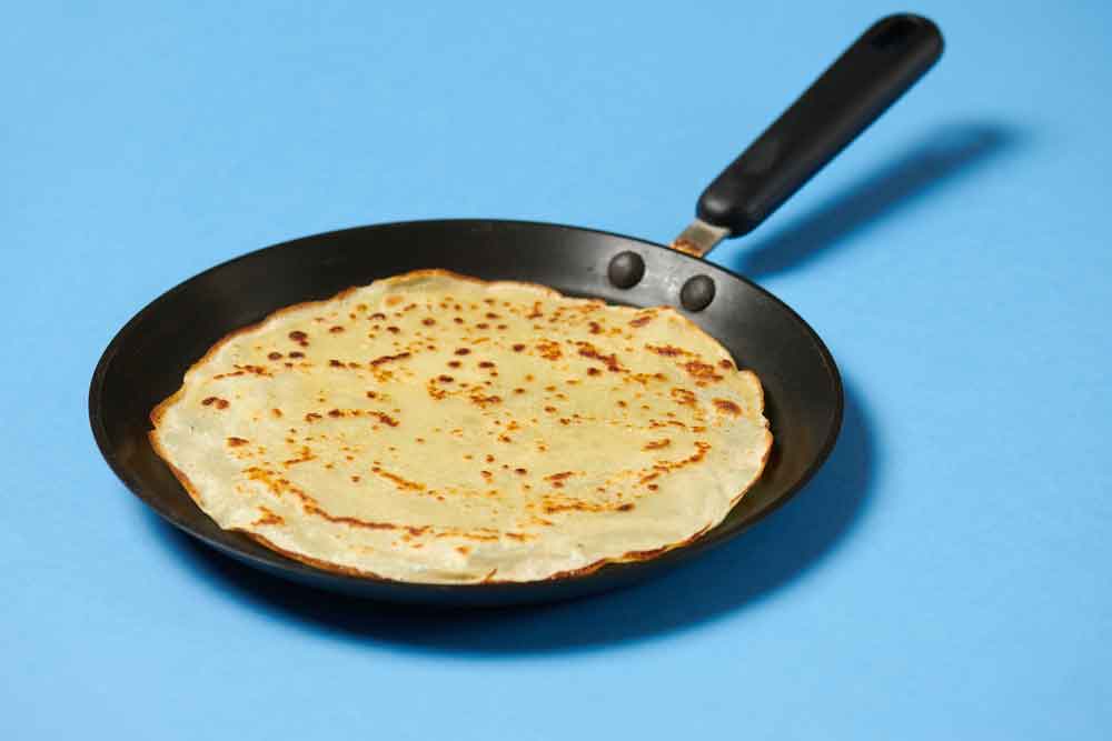 Recept voor glutenvrije, koolhydraatarme pannenkoeken. Op de foto een pannenkoek in een pannenkoekenpan.