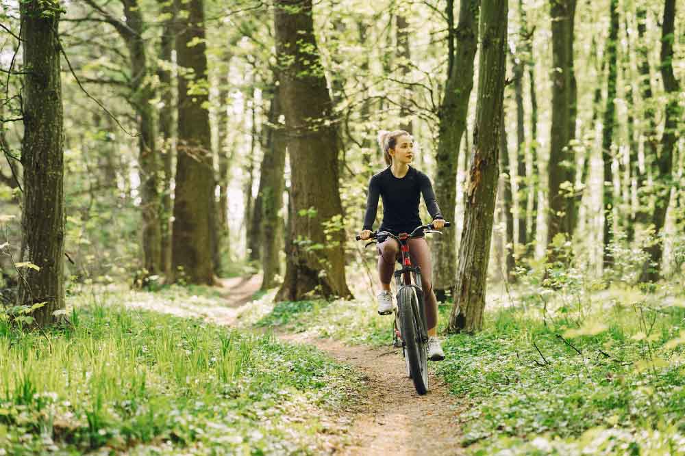 Sportieve tips voor een gezond leven (op de foto een jonge vrouw op de fiets door het bos).