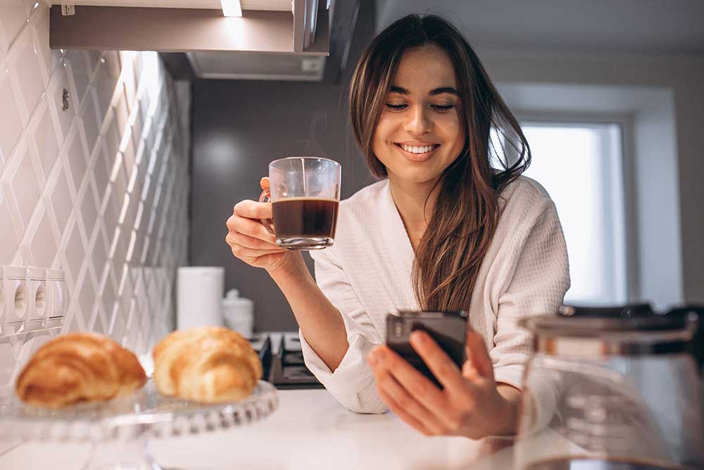 Vrouw in de ochtend tijdens het ontbijt al bezig met haar mobiele telefoon. Tips om minder tijd op je telefoon te besteden!