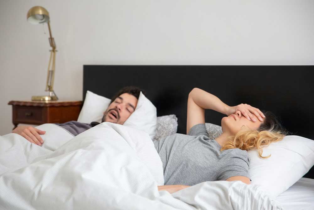Man snurkt, vrouw ligt wakker in bed. Lees de informatie en tips tegen snurken.