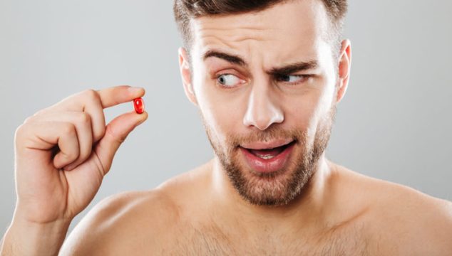 Man bekijkt een rode capsule tussen zijn vingers