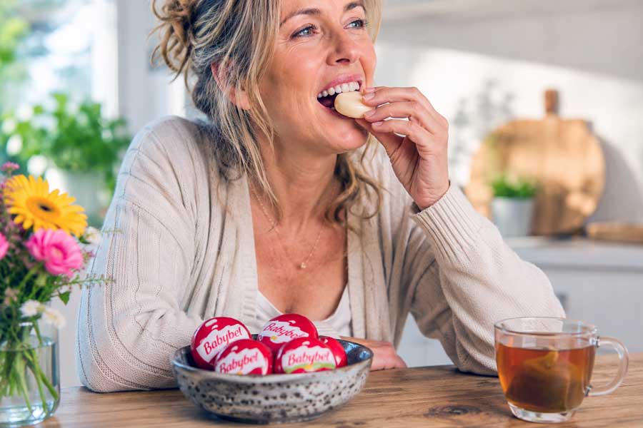 Vrouw eet aan de keukentafel een Babybel kaasje. Hoe gezond is dit?