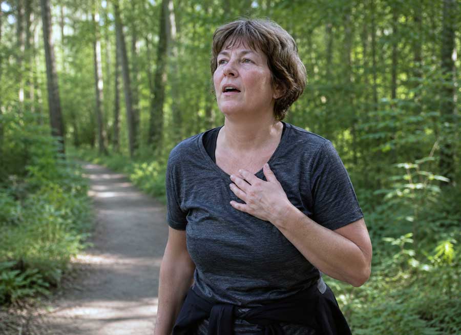 Vrouw in bos die zich benauwd voelt, terwijl ze weet dat er geen oorzaak is gevonden.