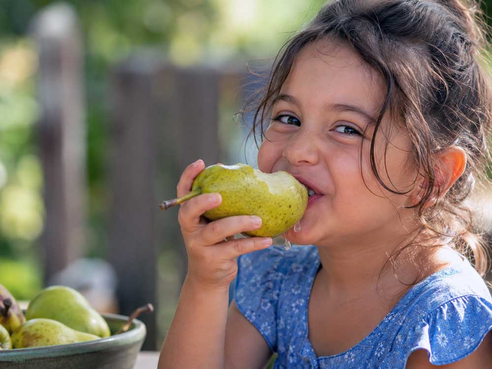 Meisje eet een peer met schil. Wat is gezonder, een peer met of zonder schil?